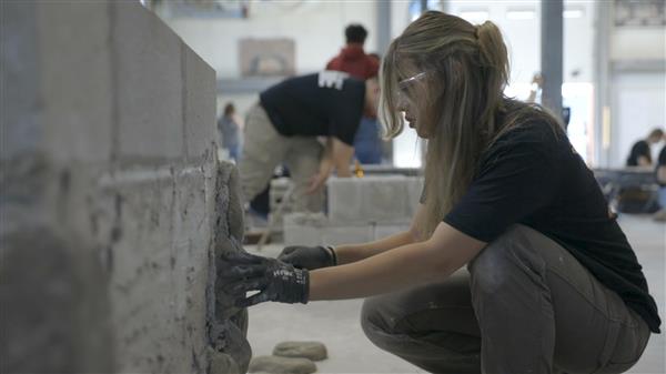 Student crouches working on masonry Student crouches working on masonry